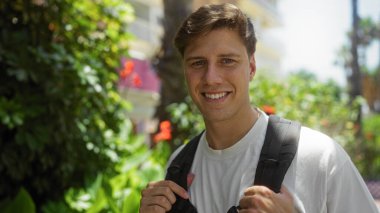 Açık havada gülümseyen genç bir adam güneşli bir günde yeşil bir parkın içinde.