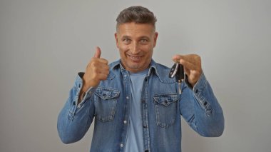 Yakışıklı, orta yaşlı bir adam arabanın anahtarlarını tutuyor ve bir portre çekiminde beyaz arkaplanda izole edilmiş bir şekilde baş parmak işareti veriyor.