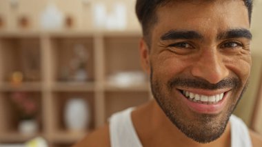 Huzurlu bir sağlık merkezinde gülümseyen genç bir adam. Arka planda ahşap raflar var. Huzurlu bir güzellik salonunda rahatlık ve mutluluk yayıyor.