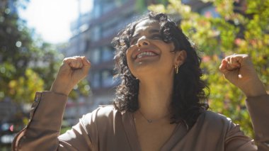 Genç, çekici, İspanyol bir kadın güneşli bir günde şehir parkında neşeli bir şekilde kutlama yapıyor..