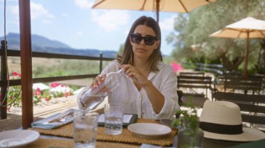 Mallorca İspanya 'daki açık hava restoranına su döken bir kadın. Güzel bir tepe manzarası ve arka planda çiçekleri var.