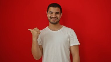 Genç, İspanyol, adamım, gülümseyen ve başparmağınla işaret eden izole edilmiş kırmızı arka plan