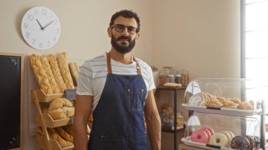 Sakallı yakışıklı, genç İspanyol bir adam fırının içinde duruyor. Etrafı yeni pişmiş ekmek ve pastalarla çevrili..