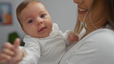 Sıcak bir yuva ortamında, sevgi dolu bir bebeği kucağında tutan kadın gülümseme ve sıcaklıkla hassas bir aile anını yakalıyor..