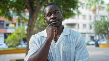 Gündüz vakti şehir parkında ağaçlar ve şehir binaları olan yakışıklı bir adam.