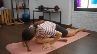 Arka planda spor malzemeleriyle yoga minderinde uzanan, aktif görünen ve esneklik egzersizi yapan kadın.