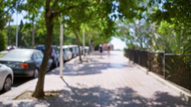 Park halindeki arabalarla kaplanmış ve arka planda bulanık insanlar olan ağaçlarla çevrili bir açık hava yolu.