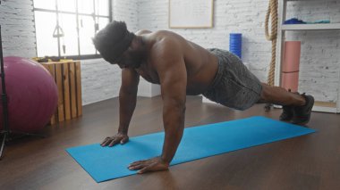 Genç, yakışıklı, Afro-Amerikalı bir adam modern kapalı bir spor salonunda, spor aletleriyle şınav çekiyor..