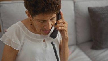 Evde oturma odasında otururken telefonda konuşan kısa saçlı yaşlı İspanyol kadın..