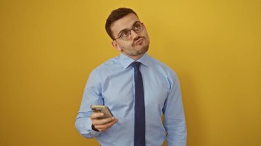 Sakallı, sarı arka planda izole edilmiş, gözlüklü ve mavi gömlekli, düşünceli, yakışıklı, İspanyol bir adam..