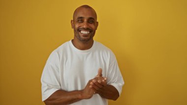 Genç Afrikalı Amerikalı adam izole edilmiş sarı arka planda alkışlıyor, modern ortamda cazibe ve neşe saçıyor.