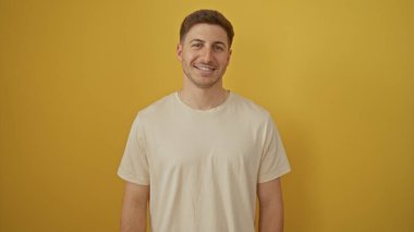 Yakışıklı İspanyol genç adam, izole edilmiş sarı bir arka plana güvenerek gülümsüyor..