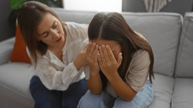 Oturma odasında genç bir kadını teselli eden kadın evde duygusal destek ve aile bağı kuruyor.