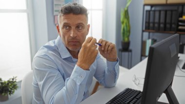 Ofis mobilyaları ve doğal ışıkla çevrili elinde kalem tutarak düşünceli ve profesyonel bir atmosfer sunan yakışıklı bir adam.