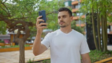 Yakışıklı, sakallı, şehir parkında selfie çeken güneşli bir günde beyaz gömlek giyen bir İspanyol..