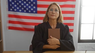 Mature woman judge in courtroom holding book with american flag in background clipart