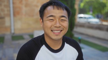 Güneşli bir günde şehir merkezinde gülümseyen yakışıklı Asyalı genç adam..