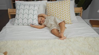Küçük kız rahat bir yatak odasında, yastıklar ve battaniyeyle uzanıyor. Evde sevimli ve sevimli bir çocukluk anı yaratıyor.