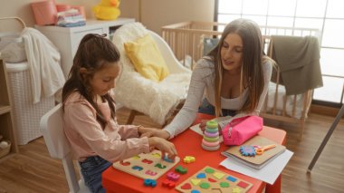 Anne ve kızı, oyuncaklarla ve öğrenme materyalleriyle çevrili ahşap zemini ve beşiği olan kapalı bir oyun odasında eğitim oyunları oynarken kaynaşıyorlar..
