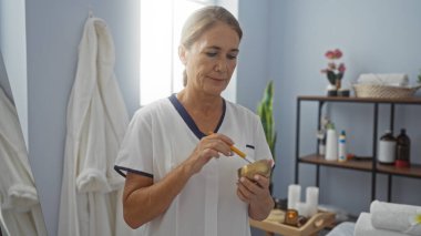 Sağlık kaplıcasında çalışan kadın, arka planda çeşitli ürünler bulunan kapalı bir güzellik merkezinde güzellik tedavisi hazırlıyor.