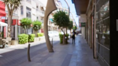 Bulanık, güneşli bir şehir caddesinde yürüyen bir kadın yeşil arka planda binalar, odaklanamadığı, odaklanamadığı bir yaz manzarası yaratıyor..