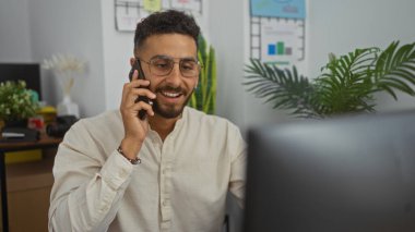 Yakışıklı, genç İspanyol bir adam ofisin içinde telefonla konuşuyor, gülümsüyor ve hevesle iletişim kuruyor..