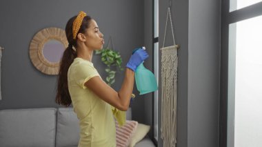 Genç bir kadın evin içinde sprey şişeyle oturma odasını temizliyor.