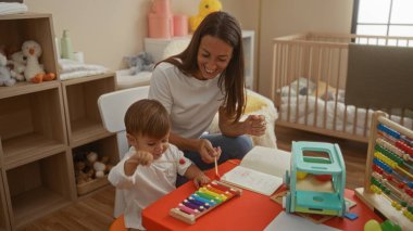 Oyuncak ve beşiğiyle rahat bir yatak odasında oynayan kadın ve oğul, kapalı alanda sevgi dolu bir aile sahnesi sergiliyor..