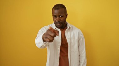 Yakışıklı, Afro-Amerikalı bir adam, izole edilmiş sarı arka planda, parmağıyla işaret ediyor.