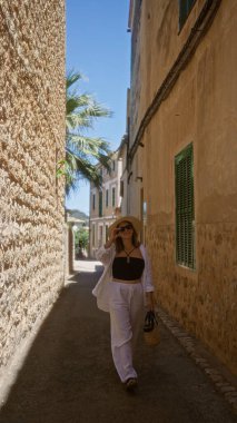 Fornalutx, Mallorca, İspanya 'da dar bir sokakta açık havada yürüyen genç bir kadın, açık mavi gökyüzünün altında saman şapkalı ve güneş gözlüklü bir yaz elbisesi giyiyordu.