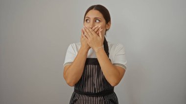 Beyaz arka planda önlük giymiş güzel esmer kadın elleri ağzını kapatmış, şaşırmış görünüyor.