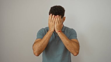 Yakışıklı genç İspanyol adam, beyaz arka planda soyutlanmış, elleriyle yüzünü kapatıyor.
