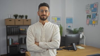 Modern bir ofiste kendine güvenen yakışıklı İspanyol bir adam. Kolları çapraz, günlük kıyafetler giyiyor..