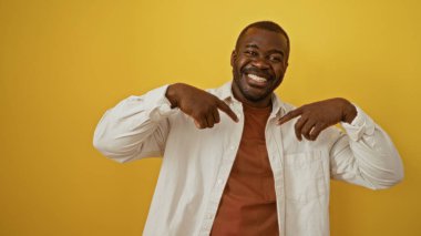 İzole edilmiş sarı arka planda gülümseyen, beyaz gömlekli, parmakları olan genç bir Afrikalı.