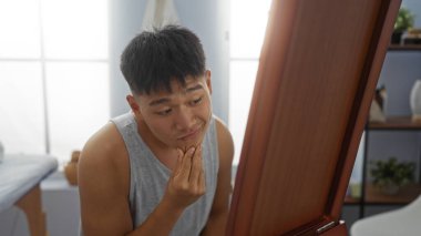 Kaplıca odasında genç bir adam modern bir iç mimariye sahip bir güzellik merkezinin aynasında yansımasına dikkatlice bakıyor.