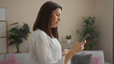 Bir şehir ortamında şık bir İspanyol kadın, akıllı telefonunu kullanıyor ve bir fincan kahveyle huzurlu bir anın tadını çıkarıyor..