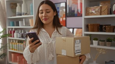 Elinde paketler olan ve dekore edilmiş bir mağazada telefon kullanan genç bir kadın.