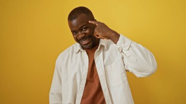 Yakışıklı genç adam izole edilmiş sarı arka planda gülümsüyor ve şakağını işaret ediyor.