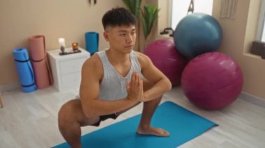 Spor aletleri ve rahatlatıcı atmosferle çevrili sağlık merkezinde yoga yapan genç bir adam..