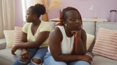 Evdeki oturma odasında oturan iki kadın birbirlerine kızgın görünüyorlar, kapalı bir aile ortamındaki duygusal gerilimi vurguluyorlar..