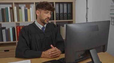 Video görüşmesi sırasında yargıç olarak çalışan genç bir adam. Arkasında kitap rafları ve belgeler var..