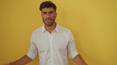 İzole edilmiş sarı arka planda beyaz gömlekli genç bir adam kendinden emin ve çekici görünüyor.