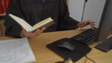 Ofis masasında elinde klavyeyle kitap okuyan cübbeli bir yargıç ve sadece kapalı bir çalışma ortamını gösteren belgeler.