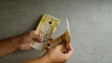 Filipin pesolarını tutan ve sayan adam, 500 pesoluk banknotları iki eliyle açıkça gösteriyor..