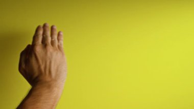 İnsan eli ve parmakları parlak sarı bir arkaplanda, yakın plan ve detaylı bir görüntü yakalıyor..