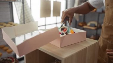 Genç adam, kapalı bir pastanede pembe bir kutuda hamur işi paketliyor.