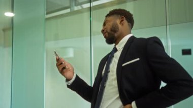 Ofisteki takım elbiseli genç adam içeride telefona bakıyor.