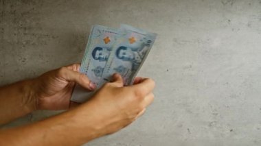 Beton arka planda Thai baht banknotları tutan adam, parmakları açıkça görülüyor..