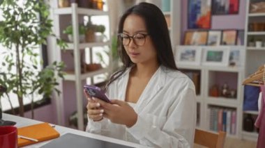 Evin içinde canlı dekorasyonlarla dolu bir evde mesaj atan bir kadın, etrafında kitaplar, sanatlar ve bitkilerle rahat bir ortam yakalıyor, modern ve rahat bir iç mekan sergiliyor..