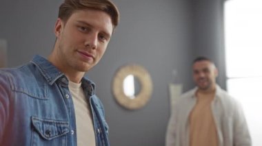 İki arkadaş, modern dekor ve doğal ışıkla rahat bir oturma odasında gülümseyen ve dans eden iki adam.